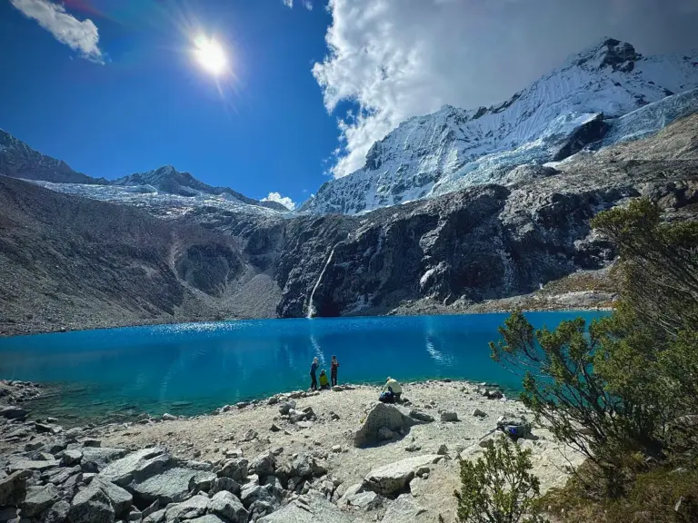 Vista de la Laguna 69 con aguas turquesas rodeada de montañas nevadas en la Cordillera Blanca de Huaraz, Perú, bajo un sol radiante.